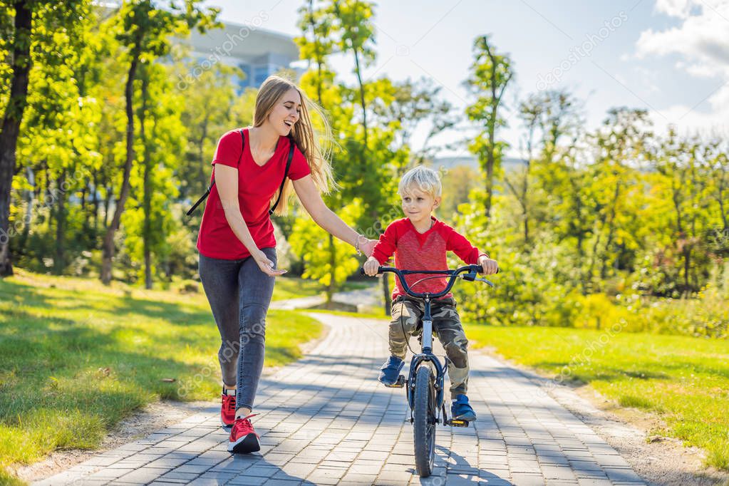 Young mother teaching son to ride bicycle in park