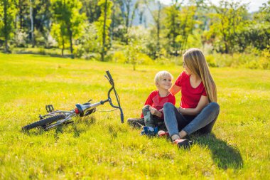 Anne ve oğlu çimenlerin üzerinde bisiklete binmek sonra dinlenme