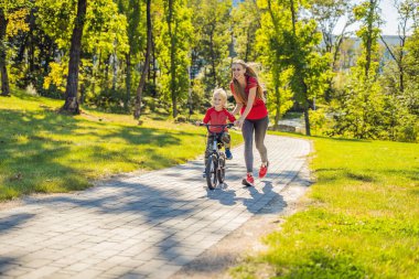 Genç Anne oğlunu parkta Bisiklete binmek kullanmayı öğretmek