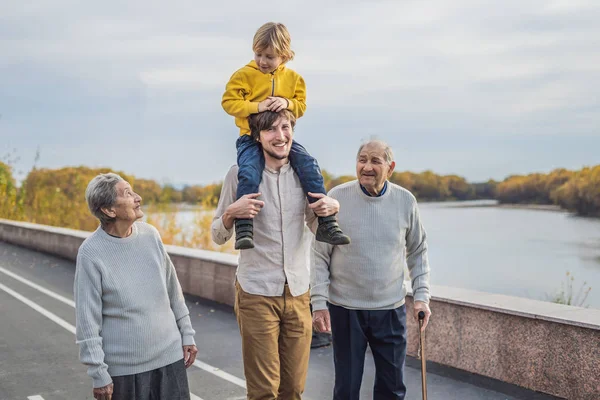 Een bejaarde echtpaar wandelingen in het park met een rivier met hun kleinzoon en achterkleinzoon — Stockfoto