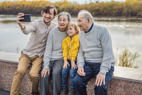 O par sênior com com neto e bisneto toma uma selfie no parque de outono. Bisavó, bisavô e bisneto — Fotografia de Stock