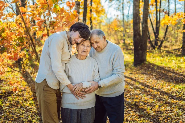 Grootmoeder, grootvader en volwassene kleinzoon knuffelen in herfst park — Stockfoto