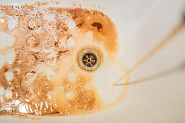Dirty brown running water falling into a white sink from tap. Environmental pollution concept