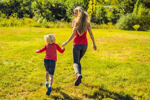 Μαμά και γιος τρέχουν στο πράσινο χορτάρι. Ευτυχισμένη οικογένεια στο πάρκο — Φωτογραφία Αρχείου