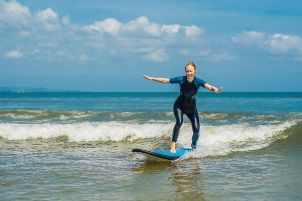 Young woman learning surfing on sea water with blue beginner surf board.