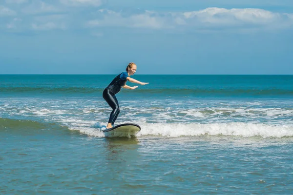 Young woman learning to surf at blue beginner surf on small sea wave at tropical vacation.