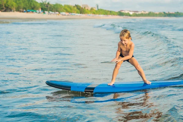 Little boy surfing on surf board on tropical beach.