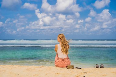 Kum üzerine oturan ve Melasti Beach, Bali Adası, Endonezya şaşırtıcı üzerinde manzarayı turkuaz su genç kadın.