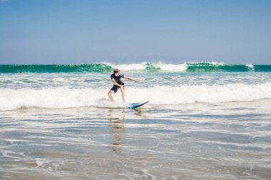 Genç Erkek sörfçü acemi surfboard köpüklü su tarafından shore Bali Adası üzerinde öğrenme.