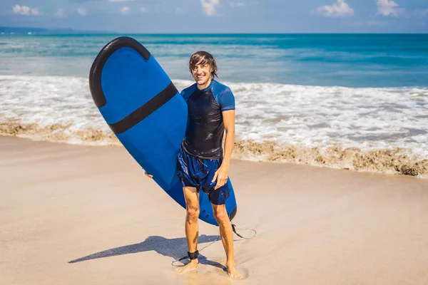 Man carrying surfboard and smiling at tropical beach.