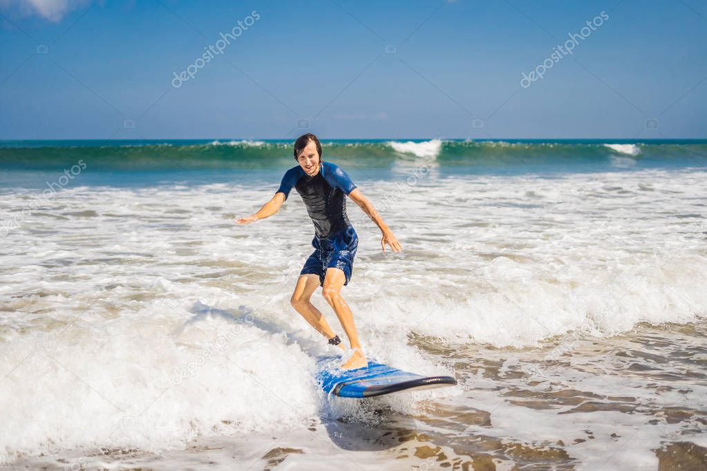 Young male surfer learning on novice surfboard in foamy water by shore of Bali island.