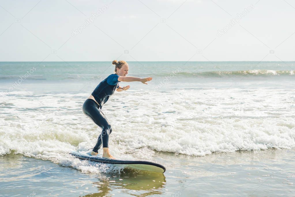Joyful young woman surfing with blue novice surfboard on small sea wave.