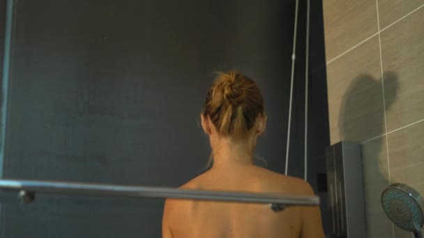 Молодая женщина принимает душ ночью с силуэтами небоскребов на заднем плане — стоковое видео