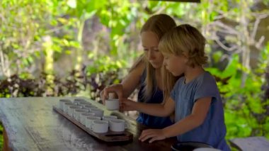Genç kadın ve küçük oğlu bir çay tadımı, degustationin tropikal bir kafe üzerinde