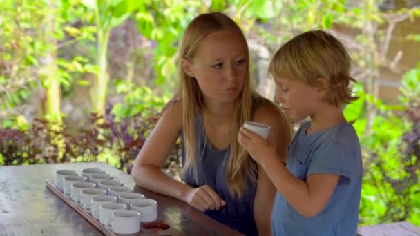 Mujer joven y su pequeño hijo en una degustación de té, degustación en un café tropical — Vídeos de Stock