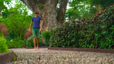 tropikal bir parkta reflexological bir yolda yürüyen bir genç adam resmini Slowmotion