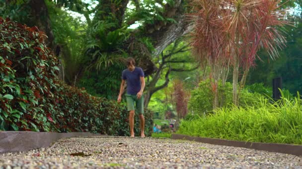 Jonge man lopen op een reflexzonemassage pad in een tropisch park — Stockvideo