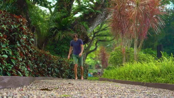 Jovem caminhando em um caminho reflexológico em um parque tropical — Vídeo de Stock