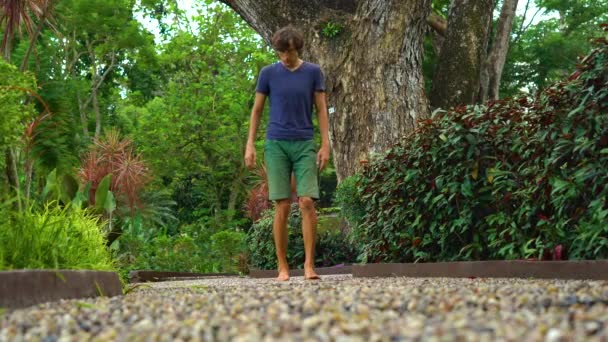 Jovem caminhando em um caminho reflexológico em um parque tropical — Vídeo de Stock