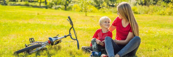 Mamma e figlio si riposano sul prato dopo aver guidato una bicicletta BANNER, FORMATO LUNGO — Foto Stock