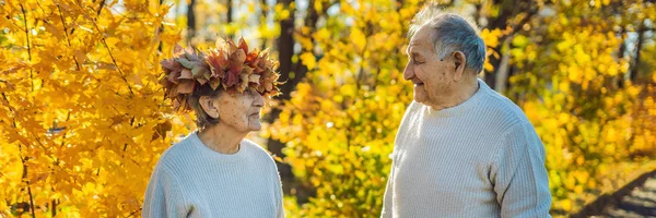 Felice vecchia coppia divertirsi al parco autunnale. Uomo anziano che indossa una corona di foglie autunnali alla moglie anziana BANNER, FORMATO LUNGO — Foto Stock