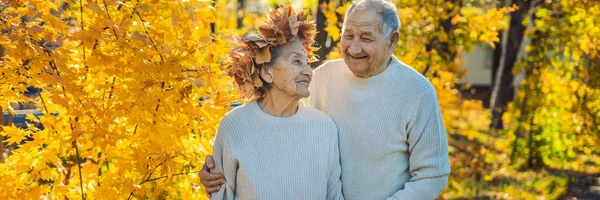 Mutlu yaşlı çift sonbahar Park'ta eğleniyor. Bir çelenk sonbaharın giyen yaşlı adam yaşlı karısı için afiş, uzun biçimde bırakır — Stok fotoğraf