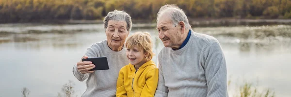 Para Starszych Biorąc Selfie Wnukiem Siedzi Jesienny Park — Zdjęcie stockowe