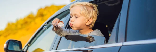 Garçon soufflant des bulles dans la fenêtre de la voiture. Voyager en voiture avec des enfants BANNER, LONG FORMAT — Photo