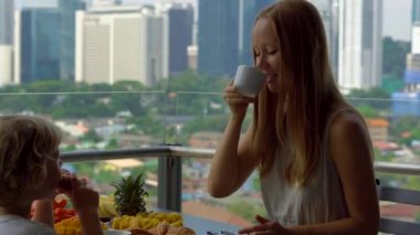 Genç kadın mürebbiye şehir merkezini gökdelenler bakan bir balkon bir çocukla kahvaltı var