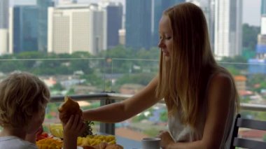 Genç kadın mürebbiye şehir merkezini gökdelenler bakan bir balkon bir çocukla kahvaltı var