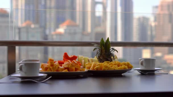 Joven institutriz preparando el desayuno en un balcón con vistas a los rascacielos del centro de la ciudad — Vídeos de Stock