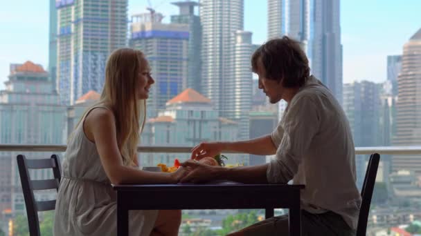 Молода жінка і чоловік поснідають на балконі з видом на хмарочоси центру міста — стокове відео