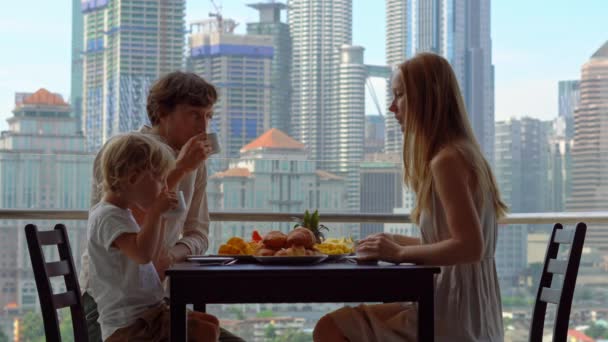 Famille prendre un petit déjeuner sur un balcon donnant sur les gratte-ciel du centre-ville — Video