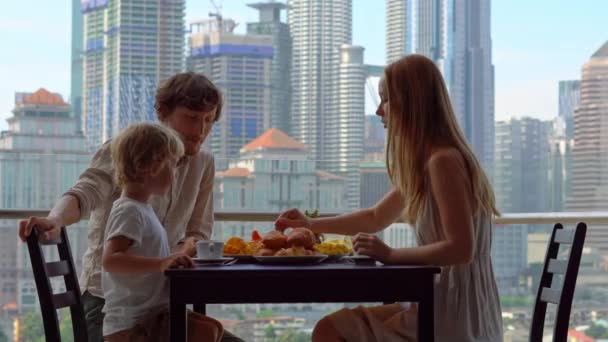 Family have a breakfast on a balcony overlooking the skyscrapers of the city center — Stock Video