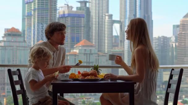 Familie genieten van een ontbijt op een balkon met uitzicht op de wolkenkrabbers van het centrum van de stad — Stockvideo