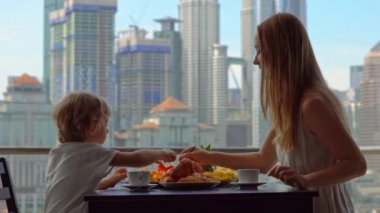 Genç kadın mürebbiye şehir merkezini gökdelenler bakan bir balkon bir çocukla kahvaltı var
