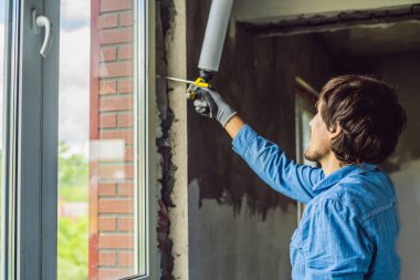 Pencere montaj sırasında montaj köpük kullanarak rahat tişörtlü genç adam. 