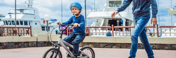 Dad teaches son to ride a bike in the park BANNER, long format