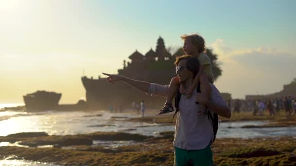 Slowmotion lövés egy apa és fia, séta a tengerpart naplemente alatt a gyönyörű Tanah Lot templom a Bali szigetén — Stock videók