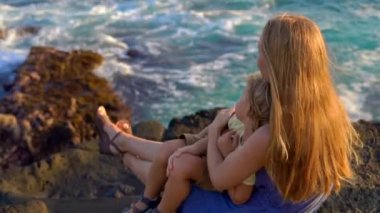 Bir anne ve oğlu bir okyanus dalgalarının yakın Tanah Lot tapınağın bakarak bir kayanın üzerine oturmuş Slowmotion atış