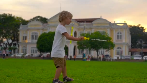 Slowmotion skott av en liten pojke som leker med en bubble blower på en torget framför Stadshuset i Georgiatown på Penang island — Stockvideo