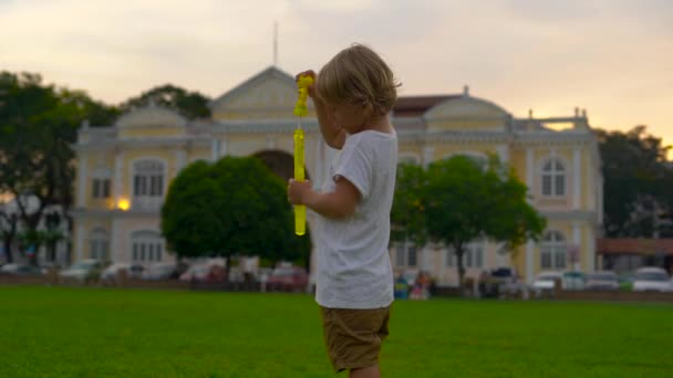 Plan au ralenti d'un petit garçon jouant avec un ventilateur à bulles sur une place devant l'hôtel de ville de Georgiatown sur l'île de Penang — Video