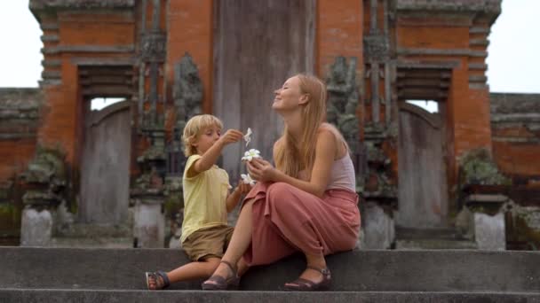 Genç bir kadın ve oğlu Bali Adası Taman Ayun Tapınağı merdivenlerde oturan el atış. — Stok video