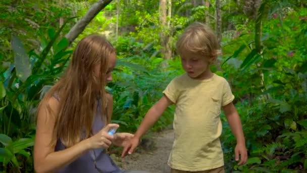 Jovem mulher na floresta tropical aplica spray de mosquito em seu filho — Vídeo de Stock