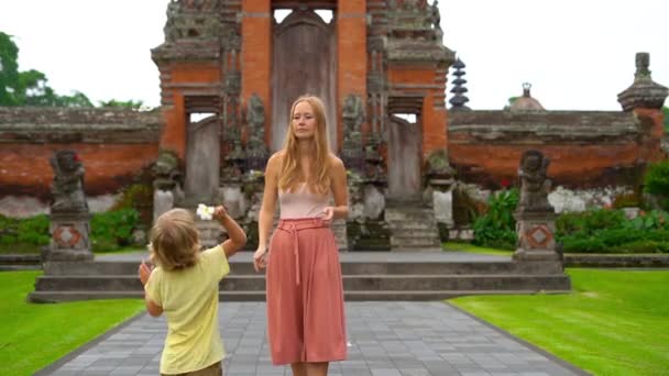 Toma en cámara lenta de una joven mujer y su hijo caminando alrededor del templo Taman Ayun en la isla de Bali — Vídeo de stock