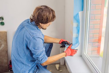 Genç profesyonel pencere montaj sırasında yapışkan bant ile çalışma.