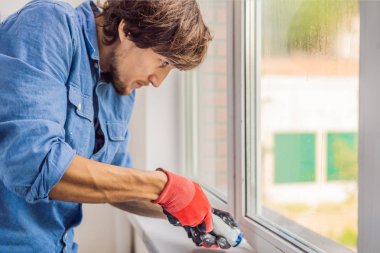 Yakışıklı delikanlı pencere montaj sırasında tutkal aracını kullanarak mavi gömlekli.