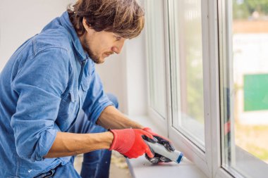Yakışıklı delikanlı pencere montaj sırasında tutkal aracını kullanarak mavi gömlekli.