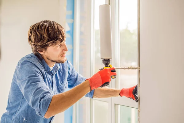 Young handyman in blue shirt using foam power tool while window installation.