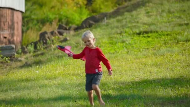 Zeitlupenaufnahme eines kleinen Jungen, der mit einem Flugzeug auf einer Wiese spielt — Stockvideo